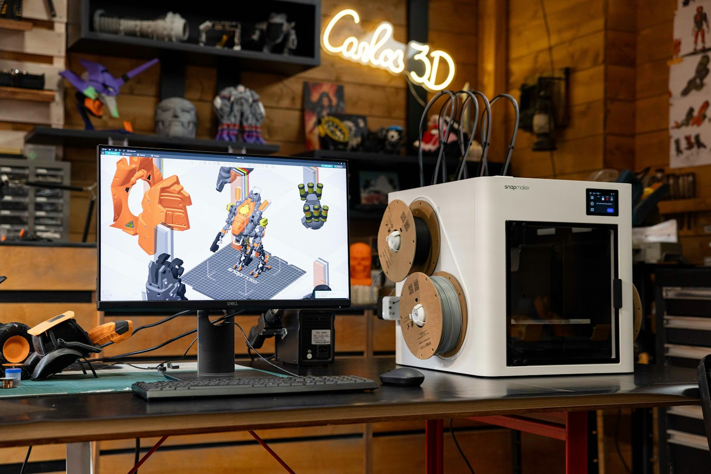 3D-skrivare och dator som visar robotmodell på träskrivbord.